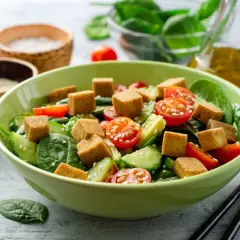 Pyszna sałatka z tofu, pomidorkami koktajlowymi, ogórkiem i szpinakiem, posypana sezamem. Idealna na lekki posiłek.