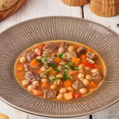 Gęsty gulasz z ciecierzycy, kawałków mięsa i marchewki, ozdobiony natką pietruszki, podany w misce.