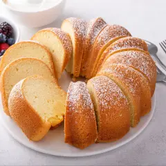 Wilgotna babka piaskowa, oprószona cukrem pudrem, czeka na talerzu z miseczką owoców leśnych. Idealna na deser.