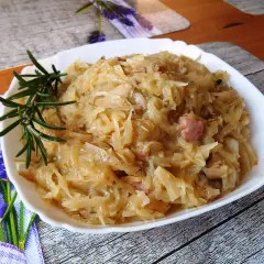 Młoda kapusta z boczkiem, aromatyczna i sycąca, podana na białym talerzu z gałązką rozmarynu.