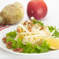 Pyszna surówka z selera z jabłkiem i orzechami, udekorowana natką pietruszki, podana z cytryną i majonezem.