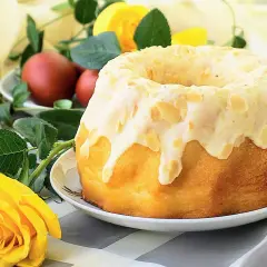 Puszysta babka z białek, polana lukrem i posypana płatkami migdałów, ozdobiona żółtą różą i pisankami.