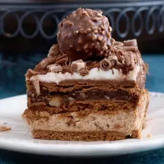 Pyszne ciasto Ferrero Rocher z warstwami czekolady, kremu i orzechów, zwieńczone całą czekoladką.