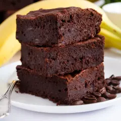 Stos puszystych brownie z bananami, ozdobiony ziarnami kawy, na talerzu z widelcem.