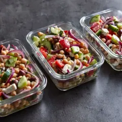 Trzy szklane pojemniki z sałatką z ciecierzycą, ogórkiem, pomidorem, fetą i czerwoną cebulą. Idealna na lunch.