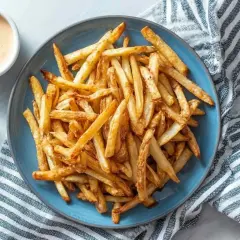Złociste, chrupiące frytki z airfryer na niebieskim talerzu, obok sosu i szklanki wody. Idealna przekąska!