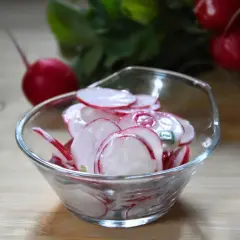Pyszna surówka z rzodkiewki w kremowym sosie, podana w szklanej miseczce. Obok leżą świeże rzodkiewki.
