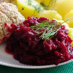 Na talerzu porcja buraczków na ciepło, obok pieczone ziemniaki i kawałek mięsa. Danie ozdobione gałązką koperku.