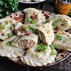 Pyszne pierogi z kaszą gryczaną, okraszone skwarkami i szczypiorkiem, na ozdobnym talerzu.
