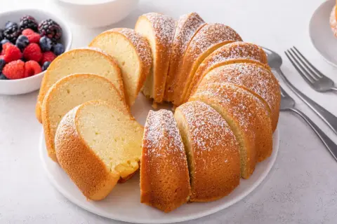 Wilgotna babka piaskowa, oprószona cukrem pudrem, czeka na talerzu z miseczką owoców leśnych. Idealna na deser.