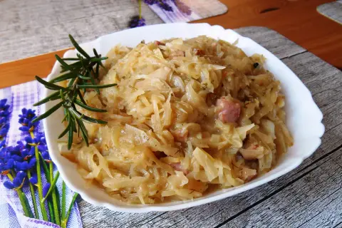 Młoda kapusta z boczkiem, aromatyczna i sycąca, podana na białym talerzu z gałązką rozmarynu.