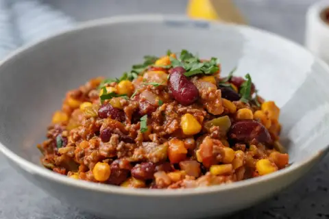 A miseczce znajduje się aromatyczne chili con carne z fasolą, kukurydzą i mielonym mięsem, posypane świeżą natką pietruszki.