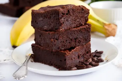 Stos puszystych brownie z bananami, ozdobiony ziarnami kawy, na talerzu z widelcem.