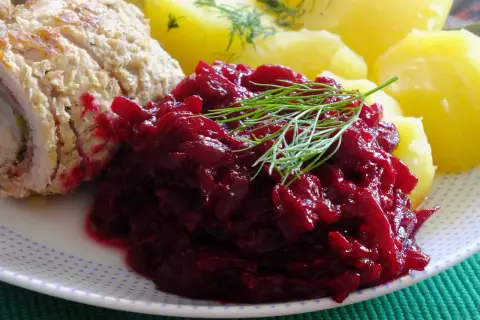 Na talerzu porcja buraczków na ciepło, obok pieczone ziemniaki i kawałek mięsa. Danie ozdobione gałązką koperku.