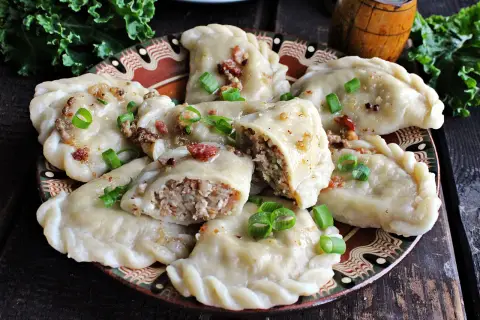 Pyszne pierogi z kaszą gryczaną, okraszone skwarkami i szczypiorkiem, na ozdobnym talerzu.