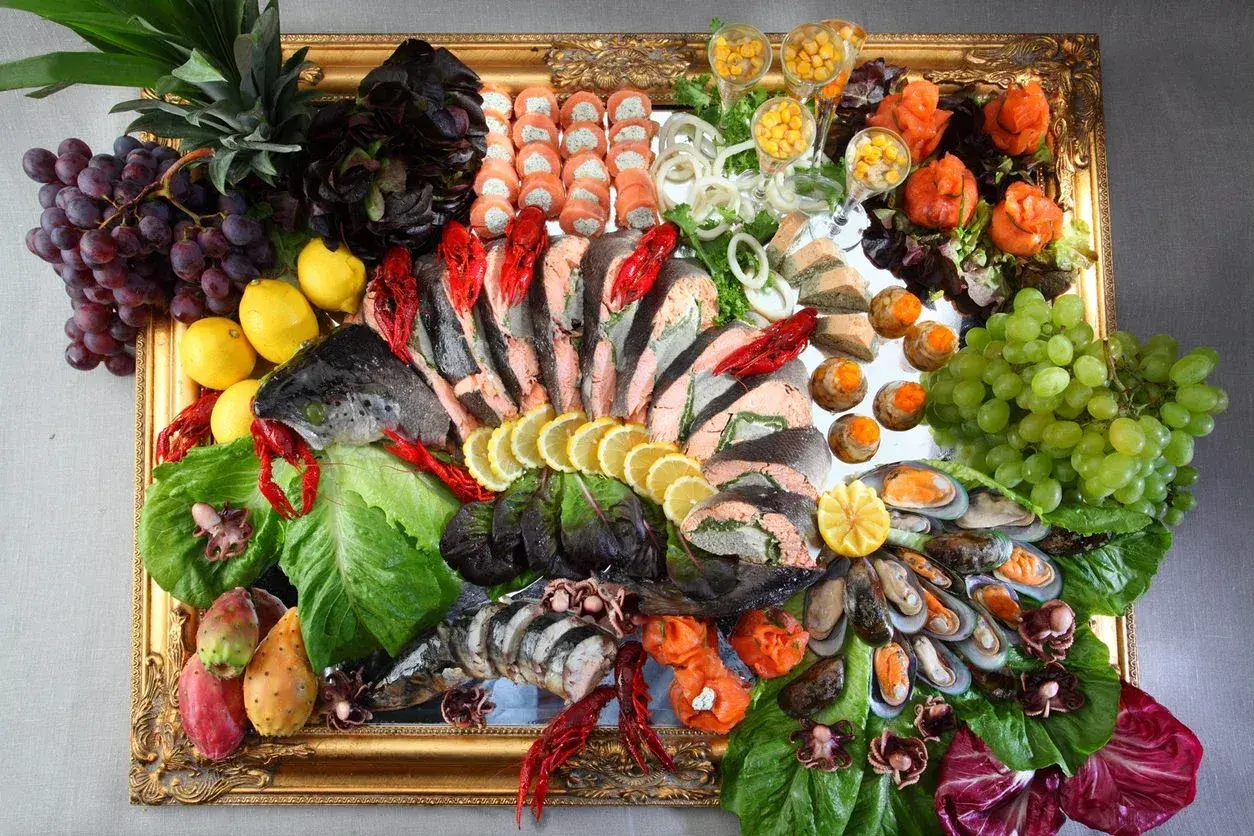 Elegancki zimny bufet przystawki na zimno na wesele: ryby, owoce morza, owoce i warzywa ułożone w złotej ramie.