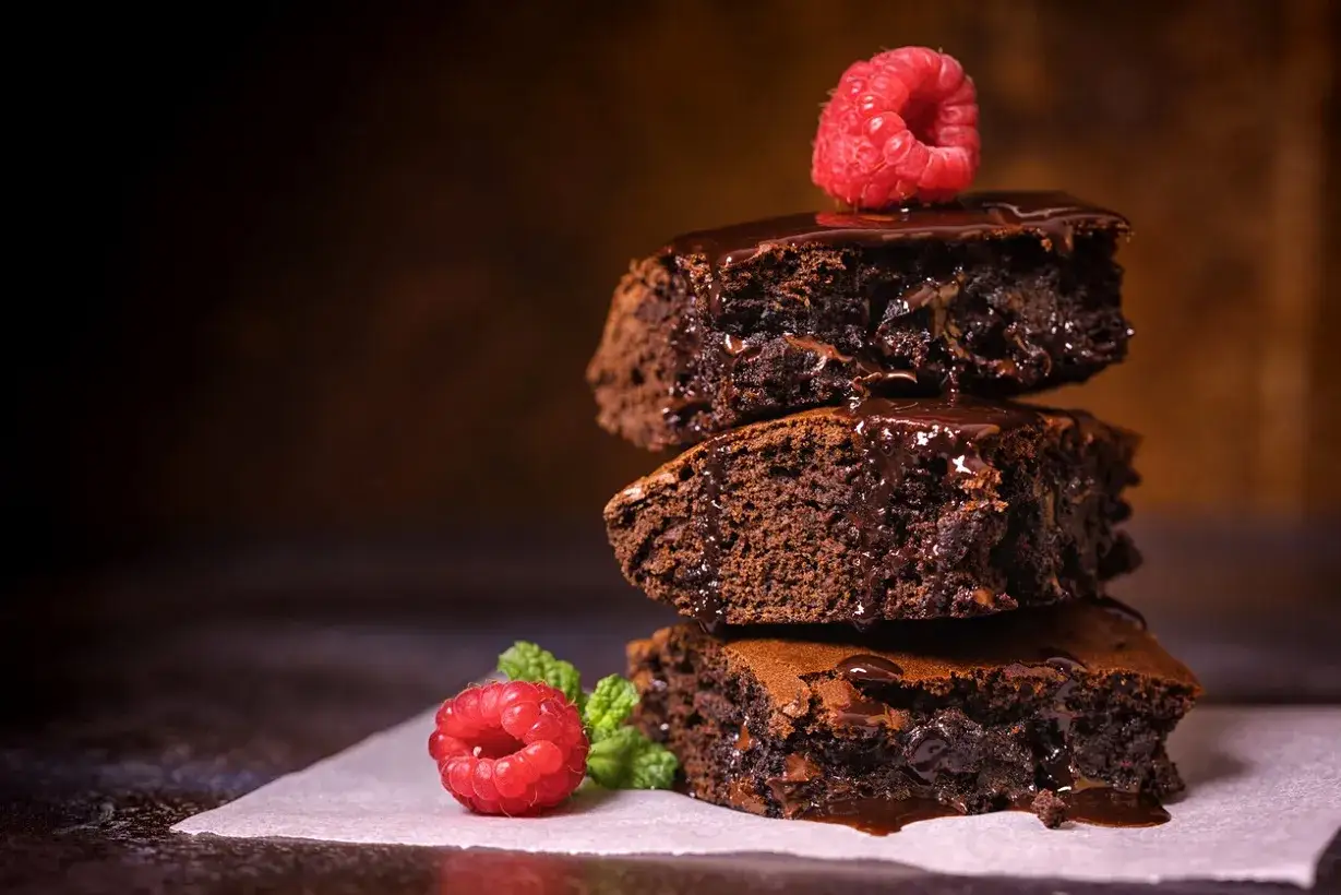 Pyszne brownie Ani gotuje, polane czekoladą i ozdobione malinami.
