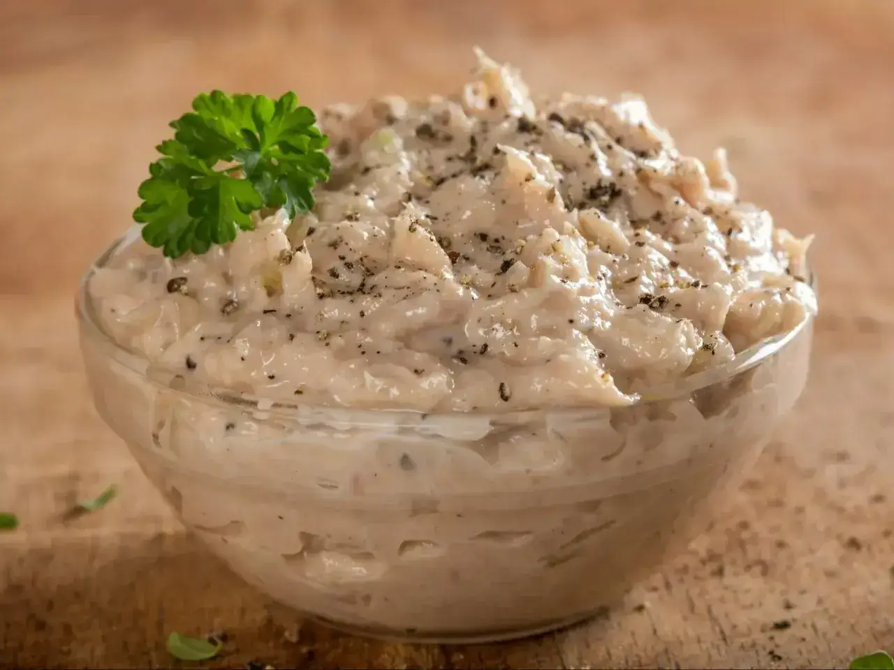 Pyszna pasta z tuńczyka w szklanej miseczce, udekorowana natką pietruszki i świeżo mielonym pieprzem. Idealna na kanapki.