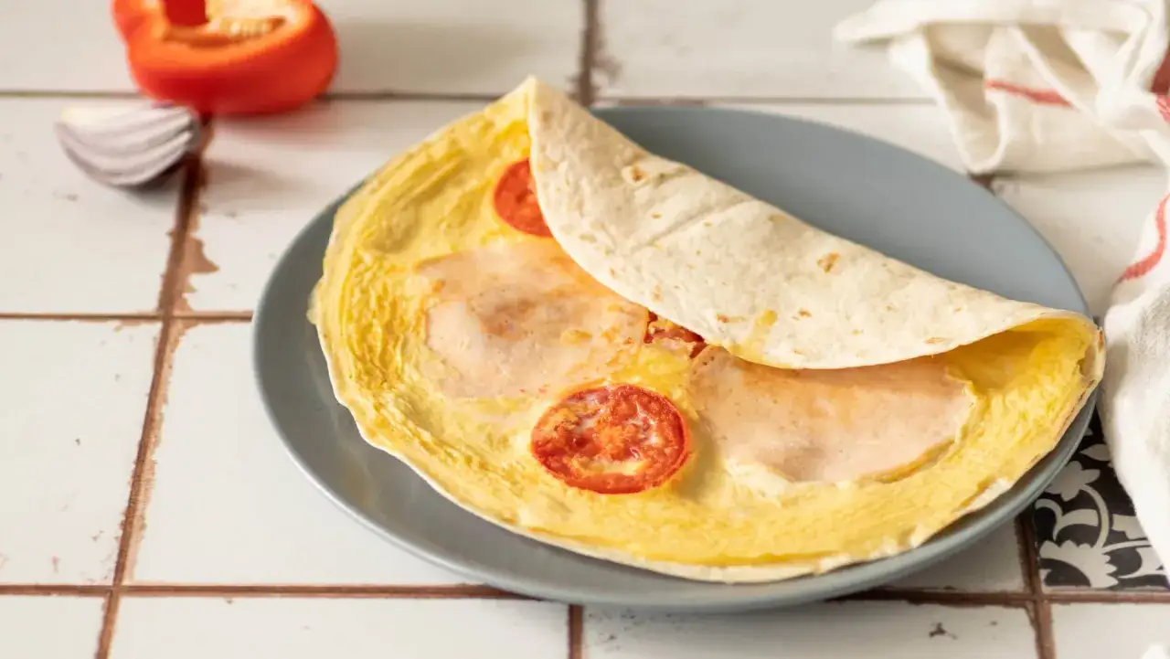 Pyszna tortilla z jajkiem, szynką i pomidorkami na talerzu. Idealna na szybkie śniadanie.