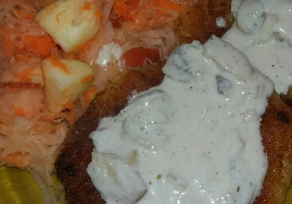 Kotlety z ziemniaków polane kremowym sosem z pieczarkami, obok surówka z kiszonej kapusty i marchewki.