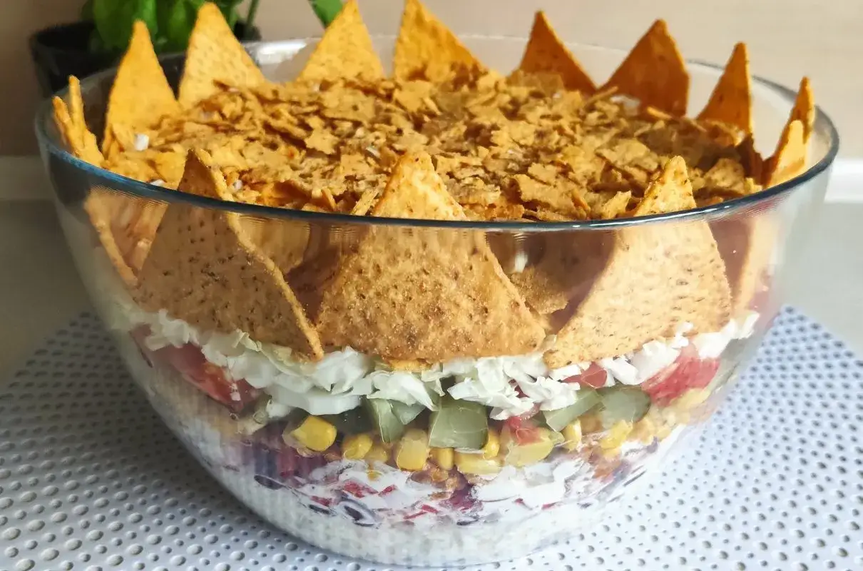 Warstwowa sałatka z nachosami, kukurydzą, pomidorami i warzywami, ozdobiona chrupiącymi chipsami.