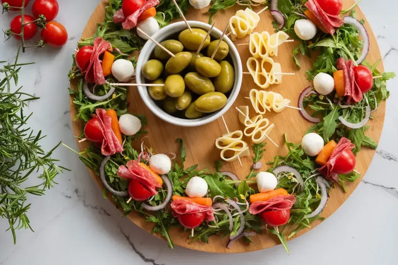 Kolorowa sałatka na imprezę: szaszłyki z pomidorkami, mozzarellą, salami i marchewką, otoczone rukolą i oliwkami.