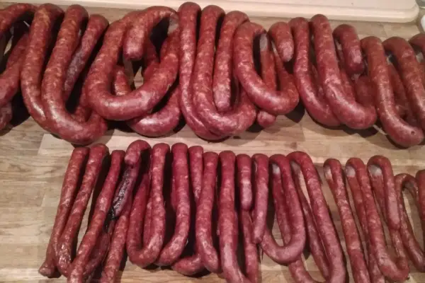 Gotowe do wędzenia, pachnące prawdziwa wiejska kiełbasa przepis. Dwie linie pętliczek z surowej kiełbasy na drewnianym blacie.