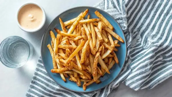 Złociste, chrupiące frytki z airfryer na niebieskim talerzu, obok sosu i szklanki wody. Idealna przekąska!